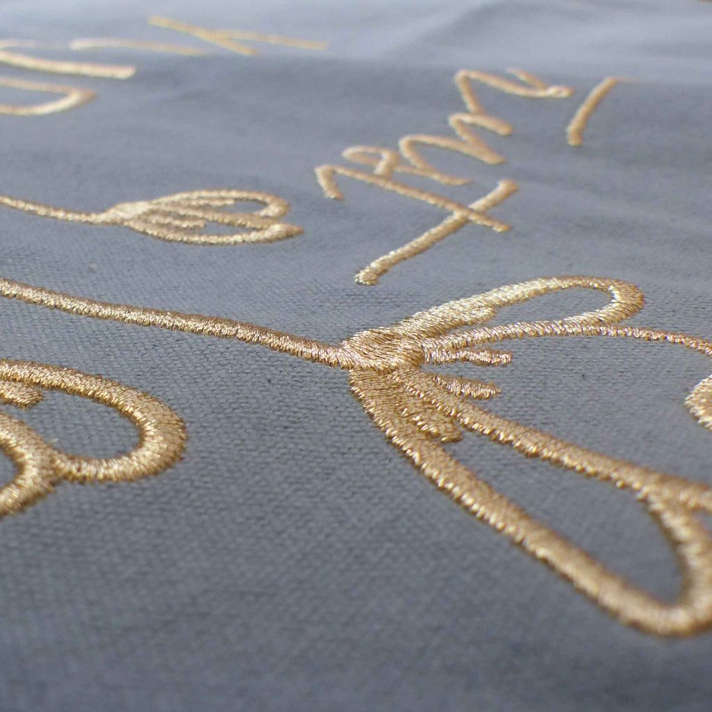 Nahaufnahme einer robusten hellblauen XL GOTS-Tote Bag aus stabilem Canvas (100% Biobaumwolle), mit Fokus auf die edel schimmernde Stickerei in gold-metallic Schriftzug Trust yourself mit minimalistischem floralen Design.
