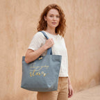 Model trägt große hellblaue Biobaumwoll-Tote Bag aus robustem Canvas mit großer Frontstickerei in goldmetallic, Schriftzug Follow your guiding star