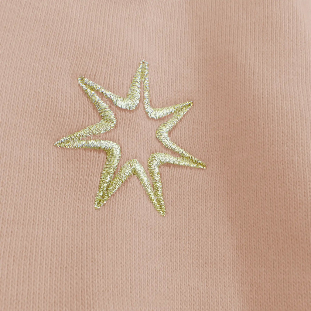Goldene Stickerei am Ärmel (siebenzackiger Stern) auf einem hellrosa Damen Sweater mit Stickerei aus Biobaumwolle.