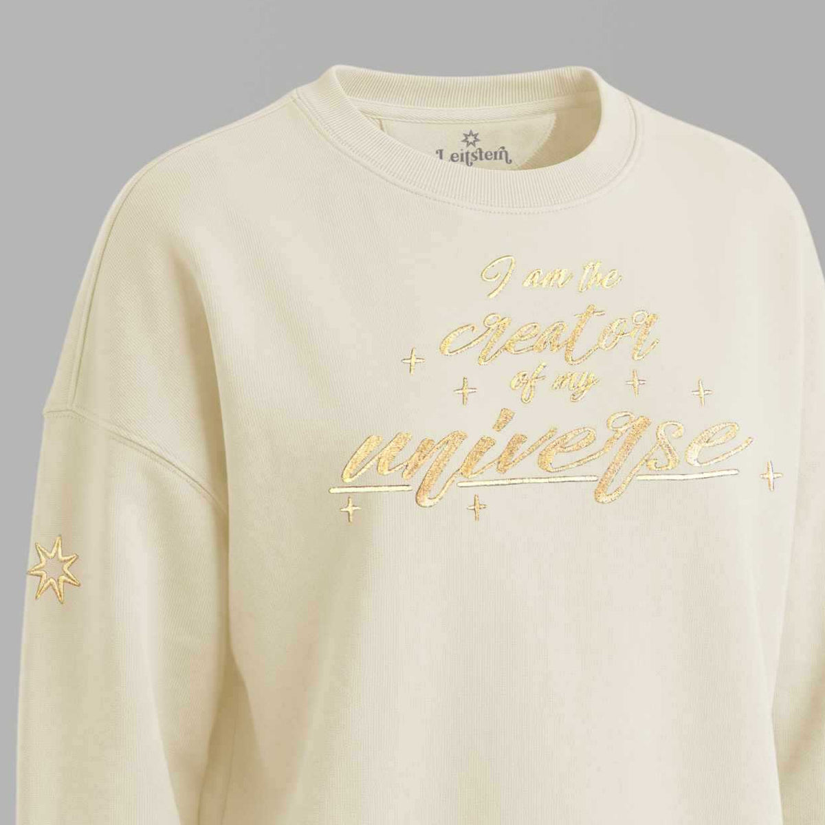 Spiritueller Damen Statement Pulli mit Affirmation aus 100% Bio Baumwolle, Farbton Natural Raw. Golden schimmernde Affirmation 'I am the creator of my universe'. Logostickerei am rechten Ärmel: Logo der spirituellen Modemarke Leitstern