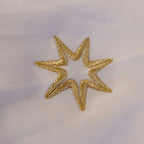 Nahaufnahme der Logostickerei (siebenzackiger Stern) am Ärmel eines nachhaltigen T-Shirts für Damen aus 100% Biobaumwolle im Farbton weiß. Es ist das Logo der spirituellen Bekleidungsmarke Leitstern.
