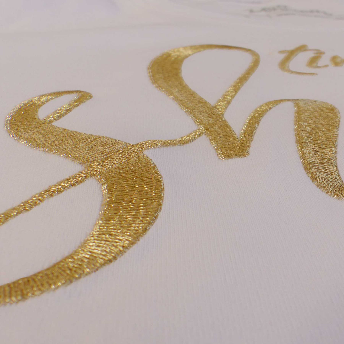 Nahaufnahme der Goldstickerei mit dem Schriftzug 'Time to shine' auf einem weißen Baumwoll T-Shirt für Damen mit Affirmation.