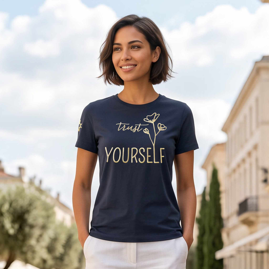 Model trägt ein dunkelblaues Damen T-Shirt aus Bio Baumwolle, mit Affirmation als große Frontstickerei in metallic-gold, Schriftzug 'Trust yourself'. Logostickerei (Stern) am rechten Ärmel.