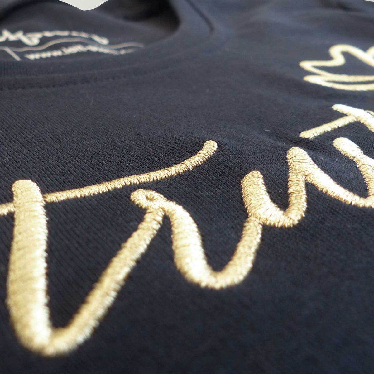 Nahaufnahme der schimmernden Goldstickerei mit dem Schriftzug 'Trust yourself' auf einem dunkelblauen Bio Damen TShirt aus reiner Baumwolle.