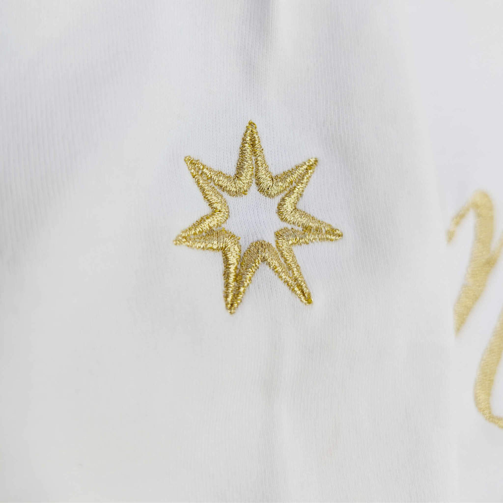 Nahaufnahme der metallic-goldenen Logostickerei am Ärmel eines weißen Bio Tshirts für Damen: siebenzackiger Stern, Symbol der Marke Leitstern.