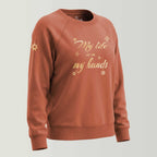 Spirituelles Damen Statement Sweatshirt mit Stickerei in gold-metallic, Sweaterfarbe terracotta. Affirmation als Frontstickerei: 'My life is in my hands'. Logostickerei am Ärmel in metallic-gold: siebenzackiger Stern, Symbol der Marke Leitstern.
