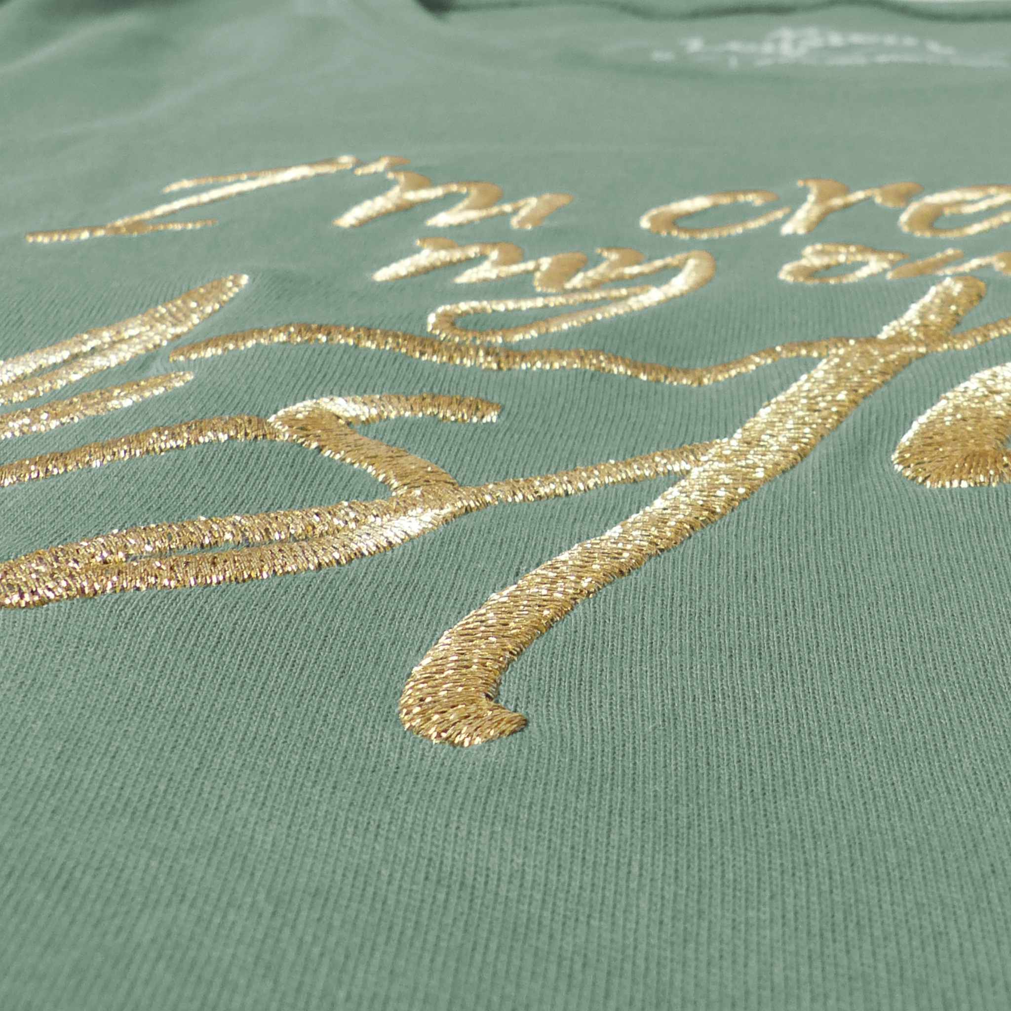Nahaufnahme eines hellgrünen Bio-Baumwollshirts für Damen aus 100% zertifizierter Biobaumwolle, Fokus auf die große edle Frontstickerei in gold-metallic I'm creating my own destiny